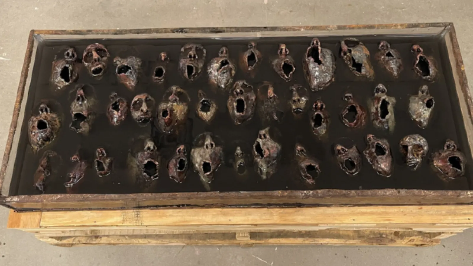 sculpture with numerous screaming faces from within a black resin material 