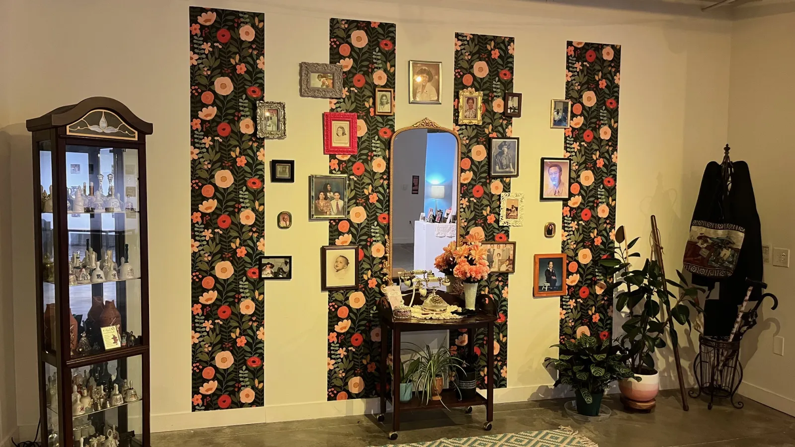 Wide shot of Crenshaw’s exhibition, featuring a family photo gallery wall, a wooden table spread, a wooden cabinet, and a coat rack.