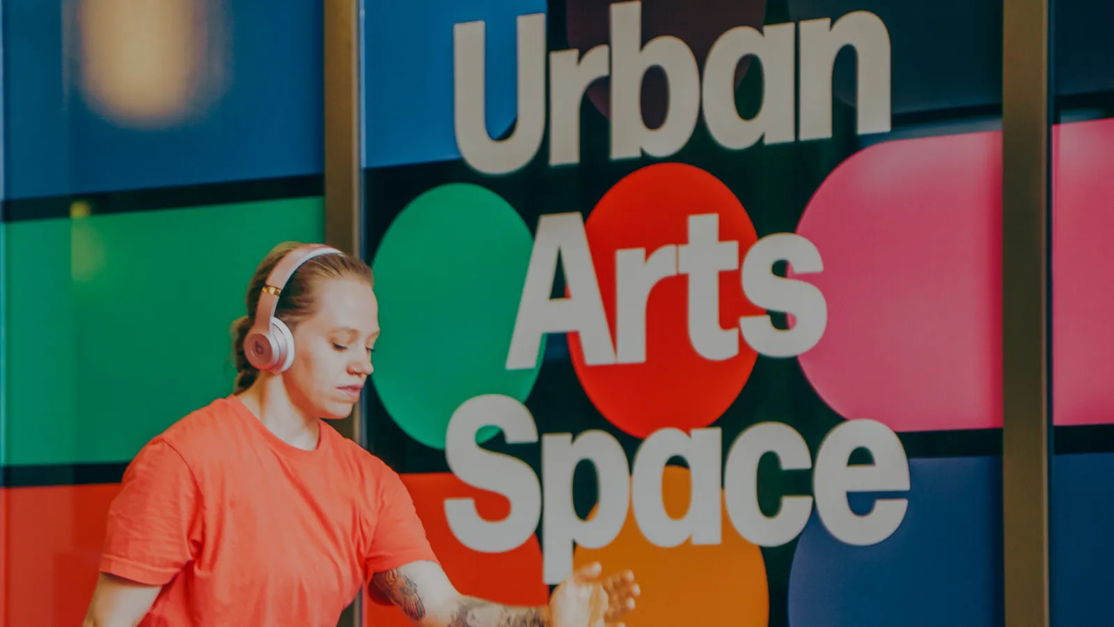 Woman walking with headphones on, in front of Urban Arts Space