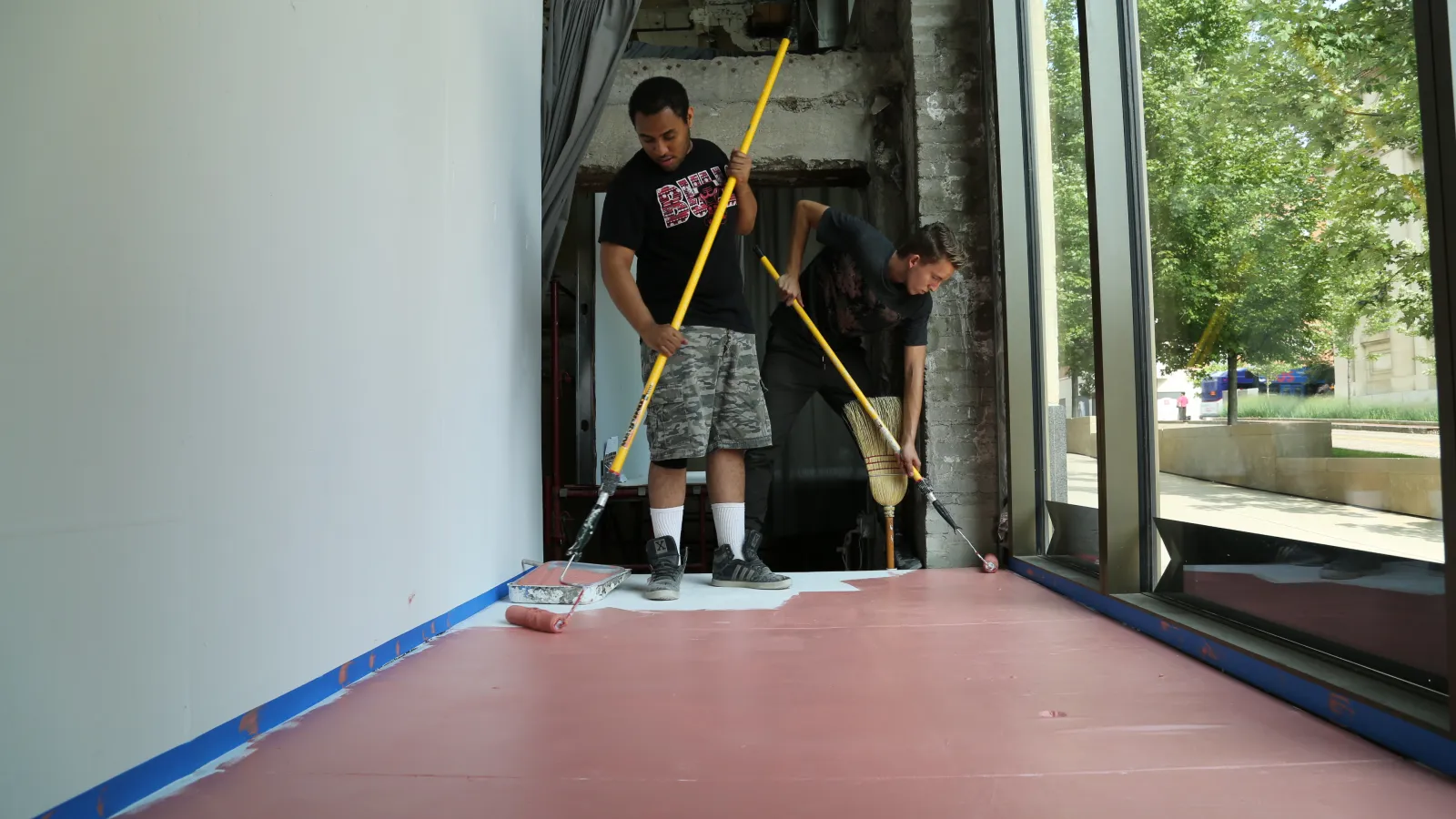 Two interns paint a window display to promote a show.