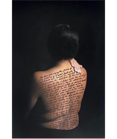 Photo of a dark-haired woman with her bare back to the camera, words written across her skin and one hand on her shoulder
