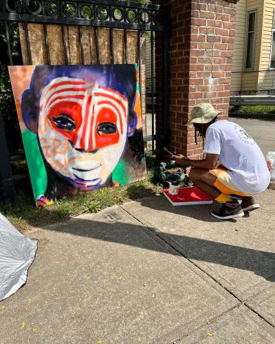 Arris's painting a square picture of a boy with traditional African face paint