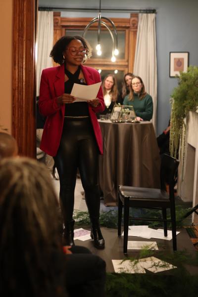 Ajanae in a red jacket standing and reading her poems