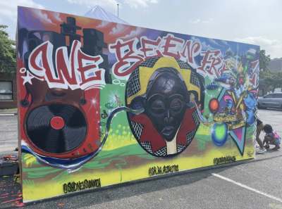 A mural in a parking lot that reads "we been fresh" and features people of color with headphones and records surrounding their face