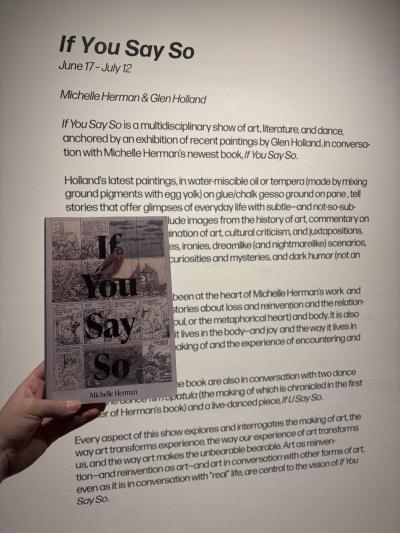 If You Say So book being held in front of an exhibition description for the If You Say So show