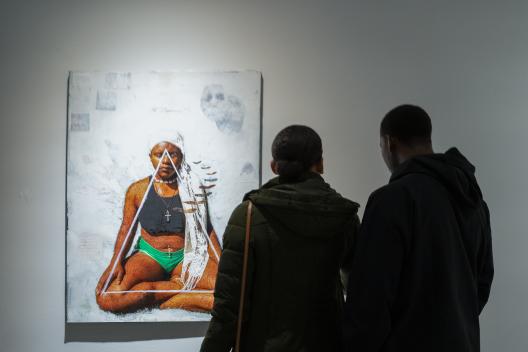 two people in front of a mixed media painting with a person sitting cross-legged