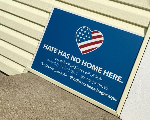 sign against yellow house that says, Hate Has No More Here" in several languages