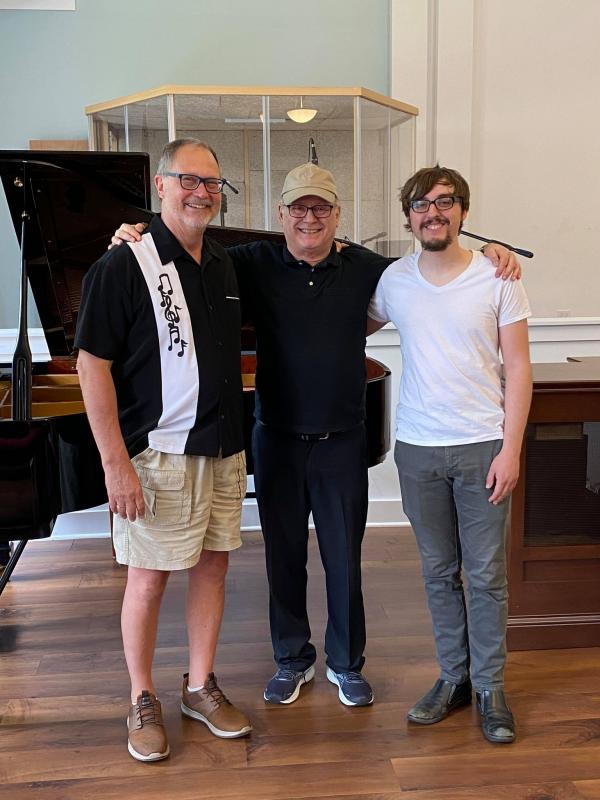 Three men standing in front of a piano 