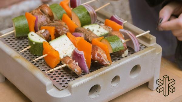 A top view of the concrete grill showing four kabobs stacked with food laying on top of a steel sheet with small holes inside the grill
