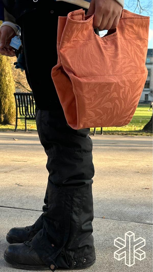 A person stands and holds an orange bag by their side.