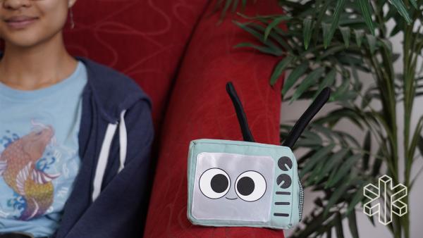 A person smiles while sitting on a chair with the cartoon TV sitting next to them.
