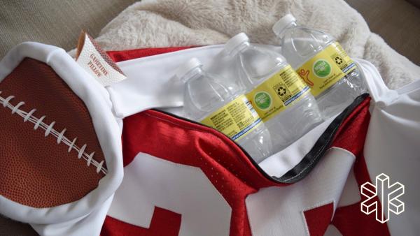 A bag made of a red jersey with white letters and a football at one end is open with a pack of water bottles inside.