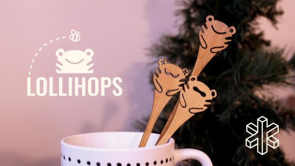 Three bamboo sticks with drawings of cartoon frogs on top are placed in a mug with a pine tree in the background.