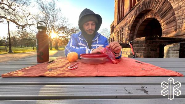 A person eats a meal set on an orange mat sitting on top of a table outdoors.