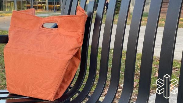 An orange bag sits on a bench outdoors.