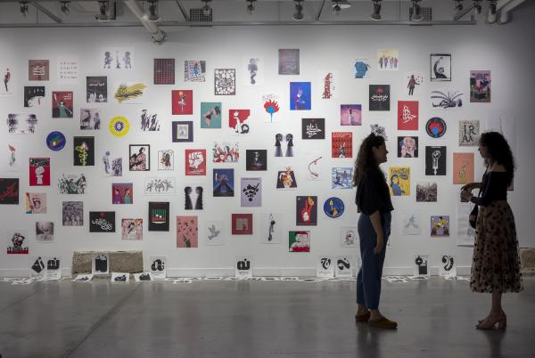 Two visitors in front of the wall of the traveling poster show by Iranian artists