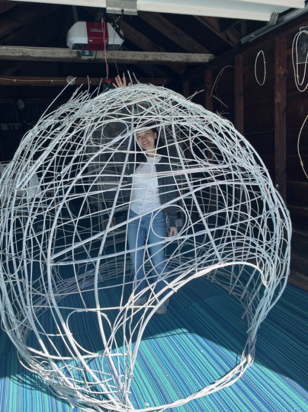 A woman standing in a giant wire hut and sculpture piece