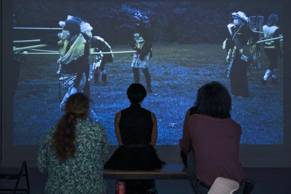 Three figures sit and watch the Spatula dance film