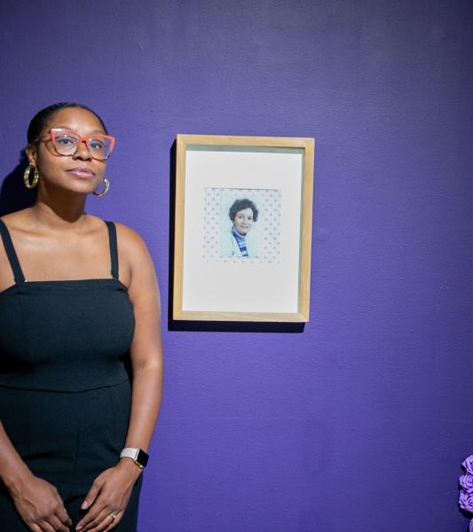 Ajanaé standing next to a photo of her great-grandmother included in her piece "Inheritance"