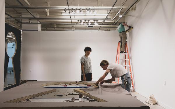 Three people work on installation in a gallery.