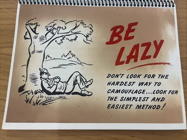 A cartoon-style drawing by Syd Solomon showing a man taking a nap under a tree. In large red letters, it reads "Be lazy". In smaller letters beneath it, it reads "Don't look for the hardest way to camouflage...look for the simplest and easiest method!"
