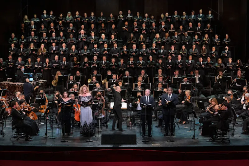 An orchestra playing onstage with a large choir singing behind them