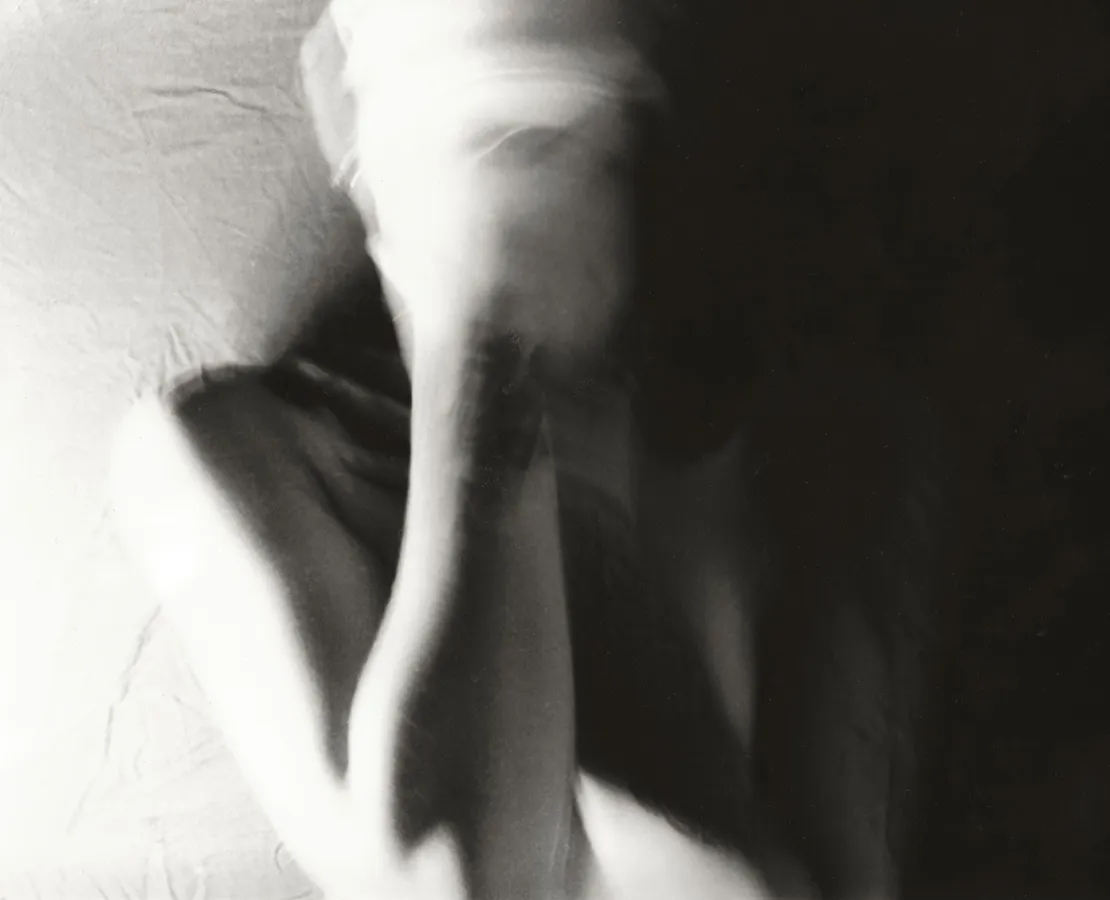 A black-and-white photo of a person with their blurred hand in front of their face