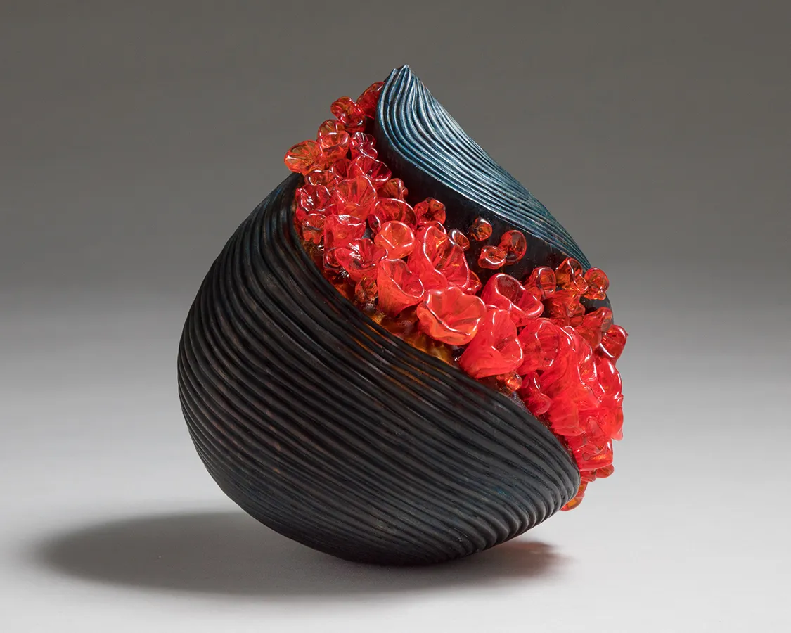 Front view of raindrop-shaped gray-blue glass sculpture with diagonal stripe of bright orange bubble-like shapes