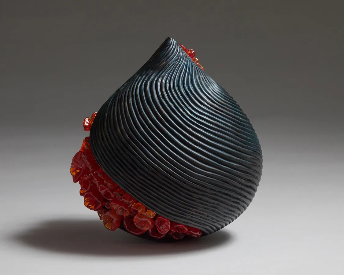 Back view of raindrop-shaped gray-blue glass sculpture with diagonal stripe of bright orange bubble-like shapes