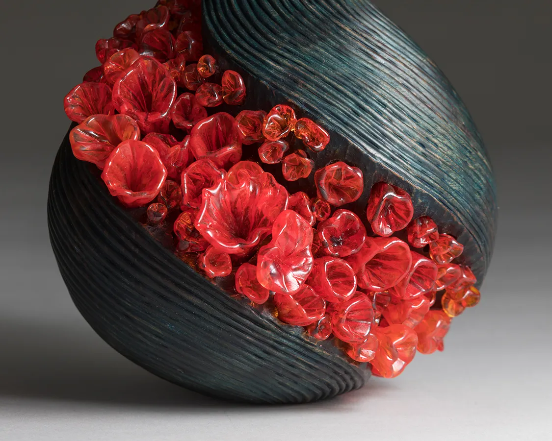 Close-up view of raindrop-shaped gray-blue glass sculpture with diagonal stripe of bright orange bubble-like shapes