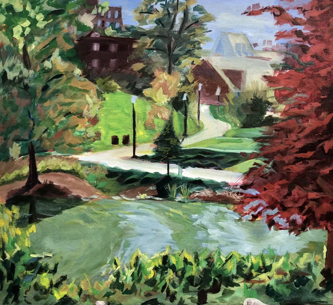 A lake surrounded by trees sits in front of a sidewalk leading to multiple buildings