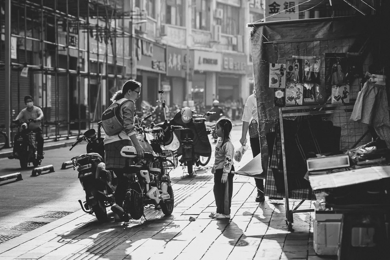 A black-and-white photograph of a mother and daughter arguing on the street in front of a market