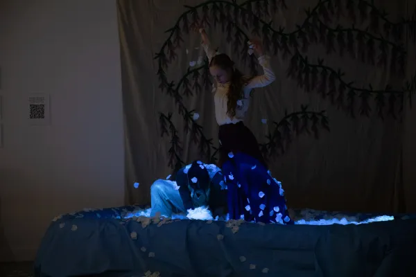 A photo of the dancers, bathed in blue light, interacting an inflatable pool full of flower petals during the performance.