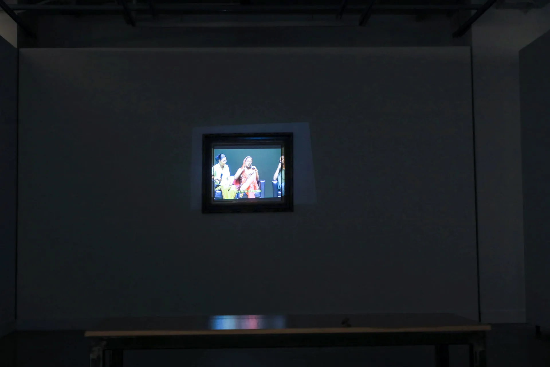 A video projected into a frame on the wall with a bench to sit on.