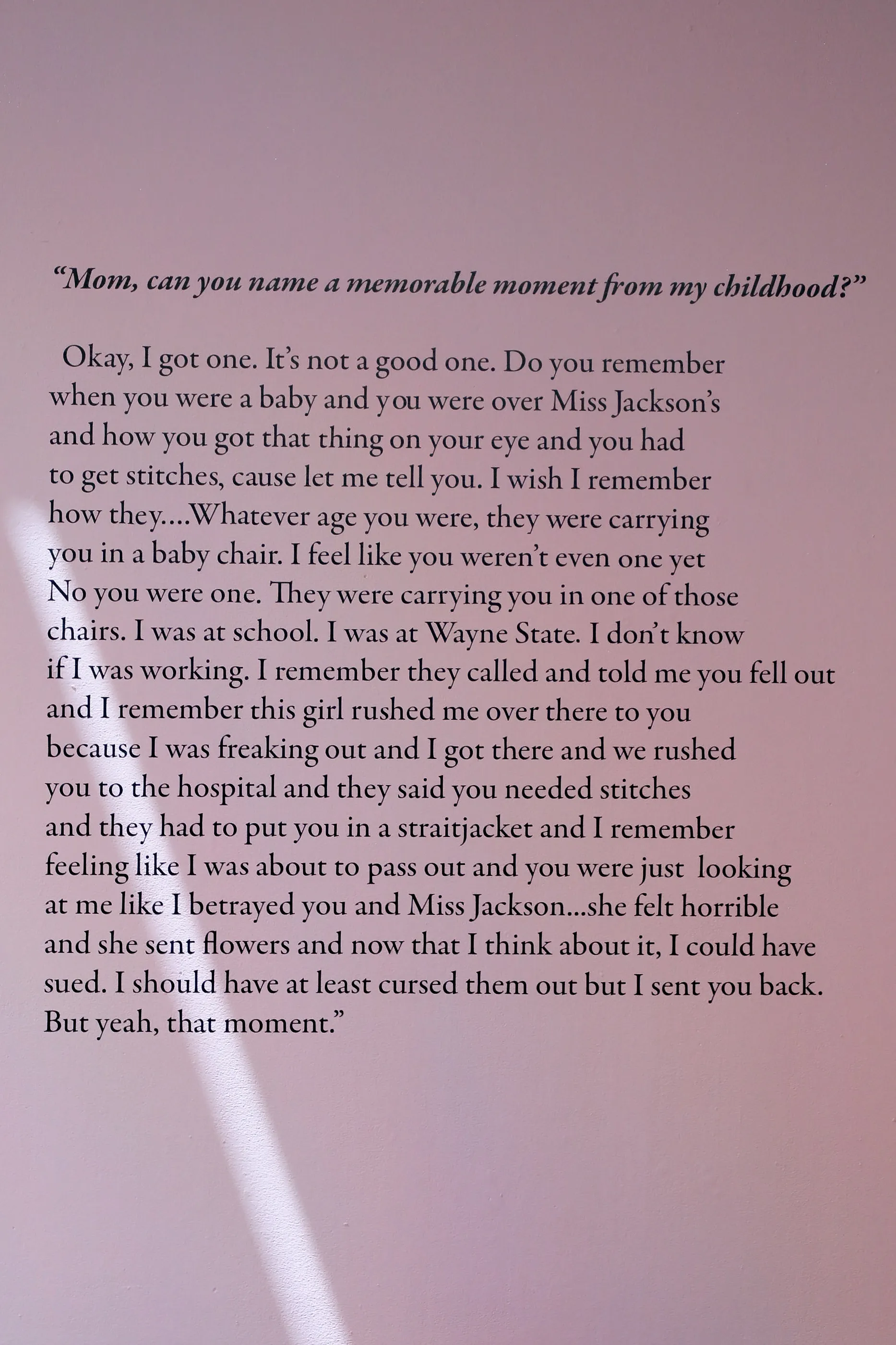 A pink wall with an excerpt of an interview with Ajanaé and her mother. The excerpt says, “Mom, can you name a memorable moment from my childhood? Okay, I got one. It’s not a good one. Do you remember when you were a baby and you were over Miss Jackson’s and how you got that thing on your eye and you had to get stitches, cause let me tell you. I wish I remember how they….Whatever age you were, they were carrying you in a baby chair. I feel like you weren’t even one yet No you were one. They were carrying yo