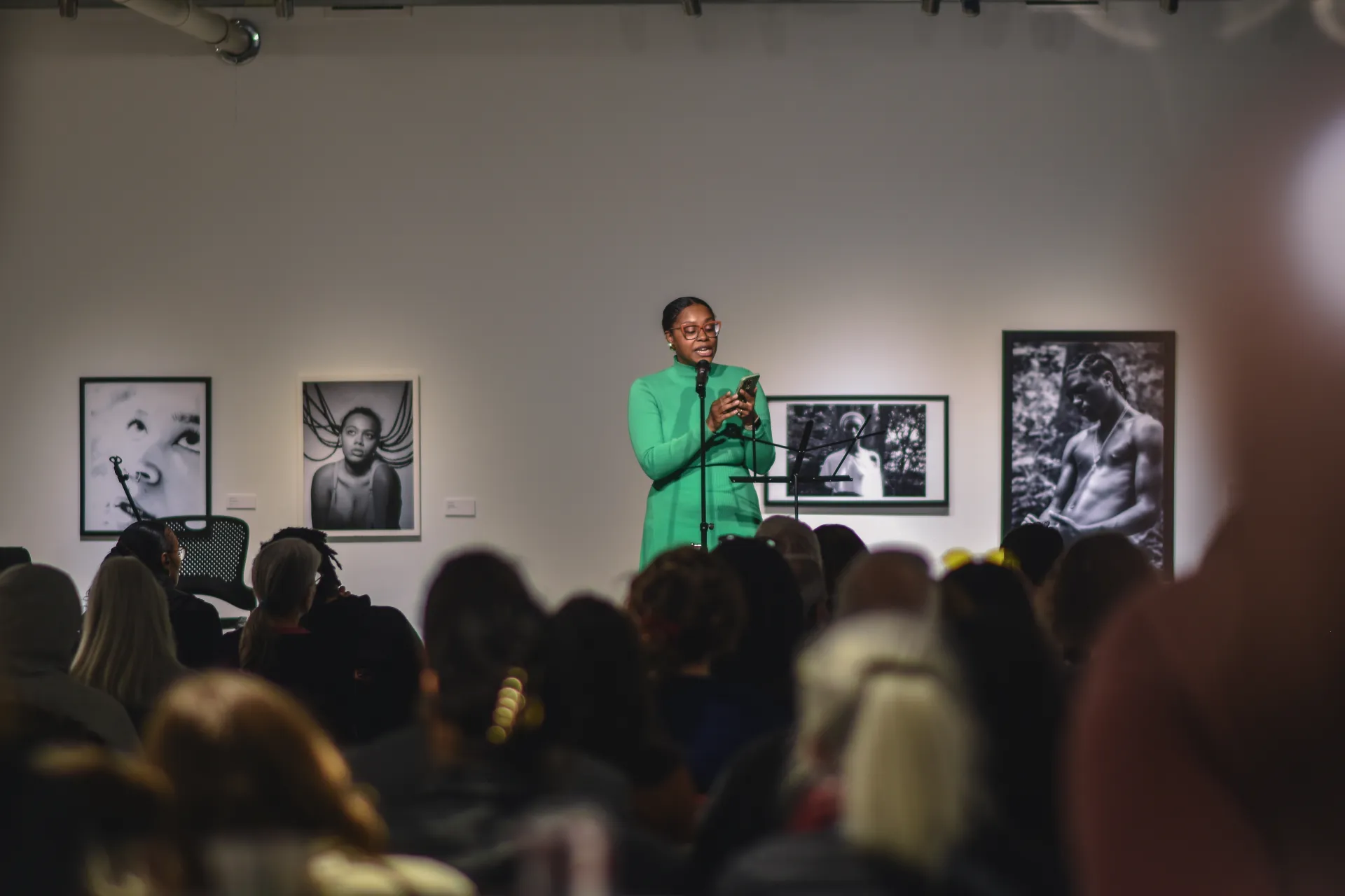 Ajanae in a green dress speaking to a crowd of people in the gallery
