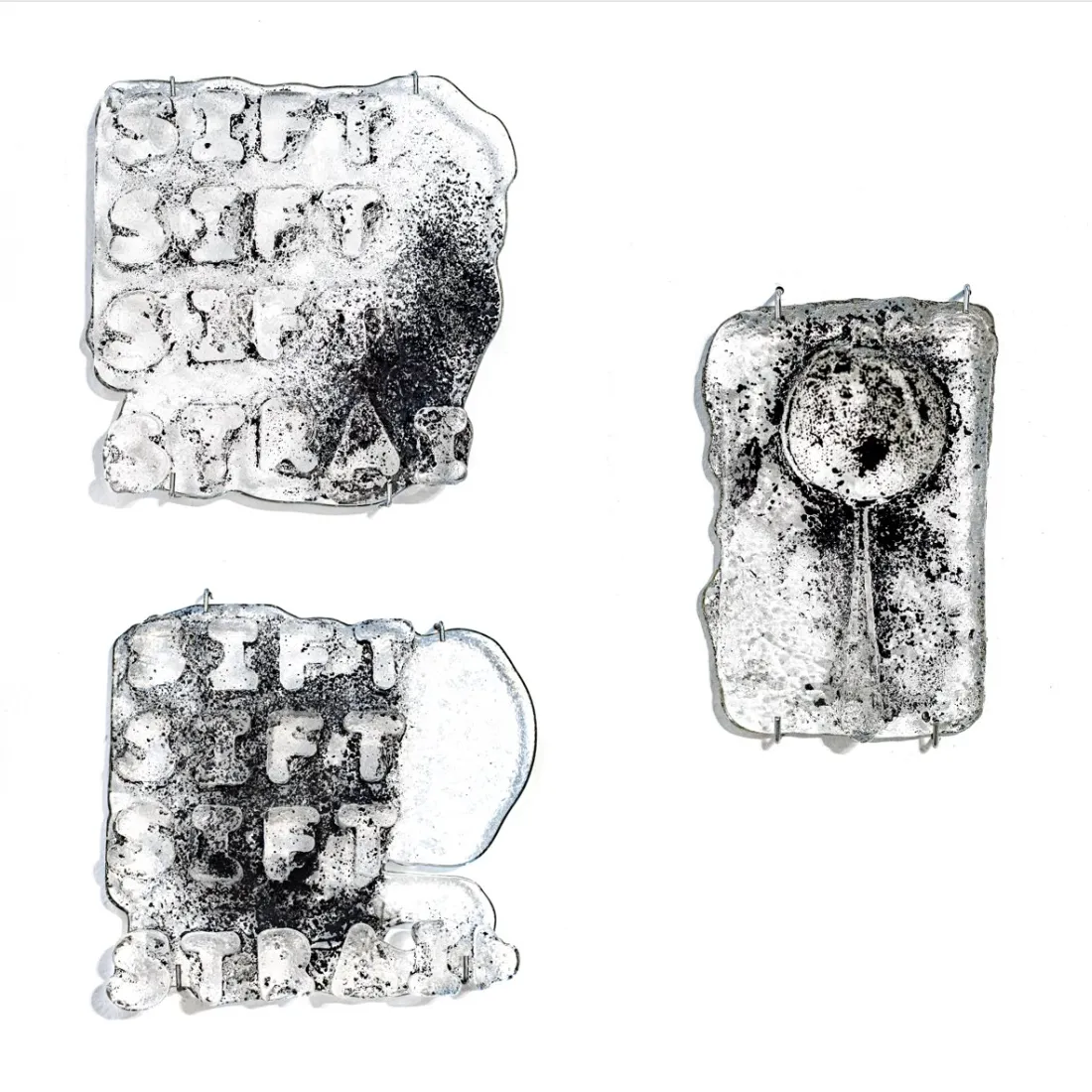 A glass sculpture stained with charcoal that reads "Sift, Sift, Sift, Strain"