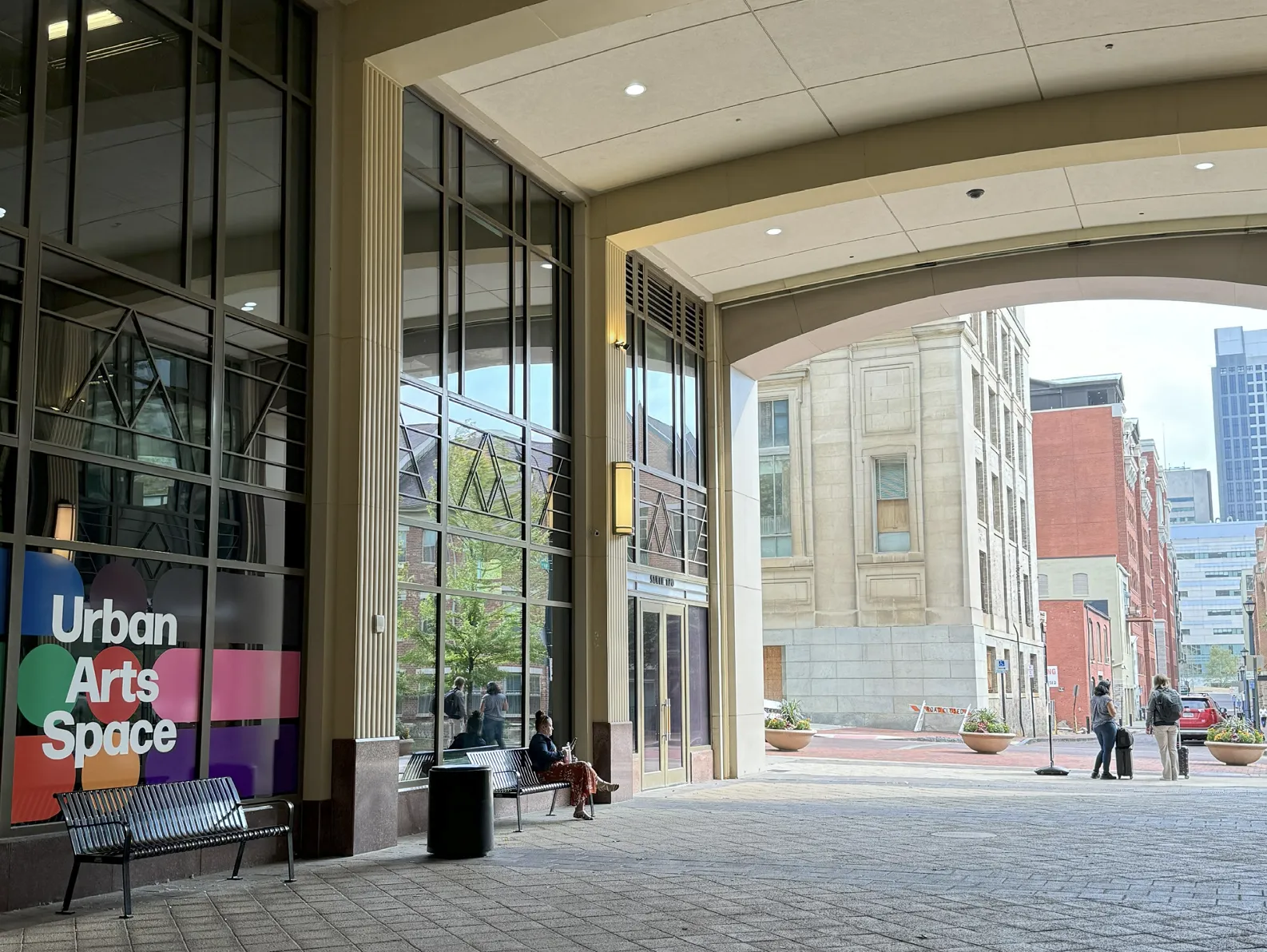 The outside of Urban Arts Space with the gallery name written on the wall in front of large colorful dots and a brief view of the city