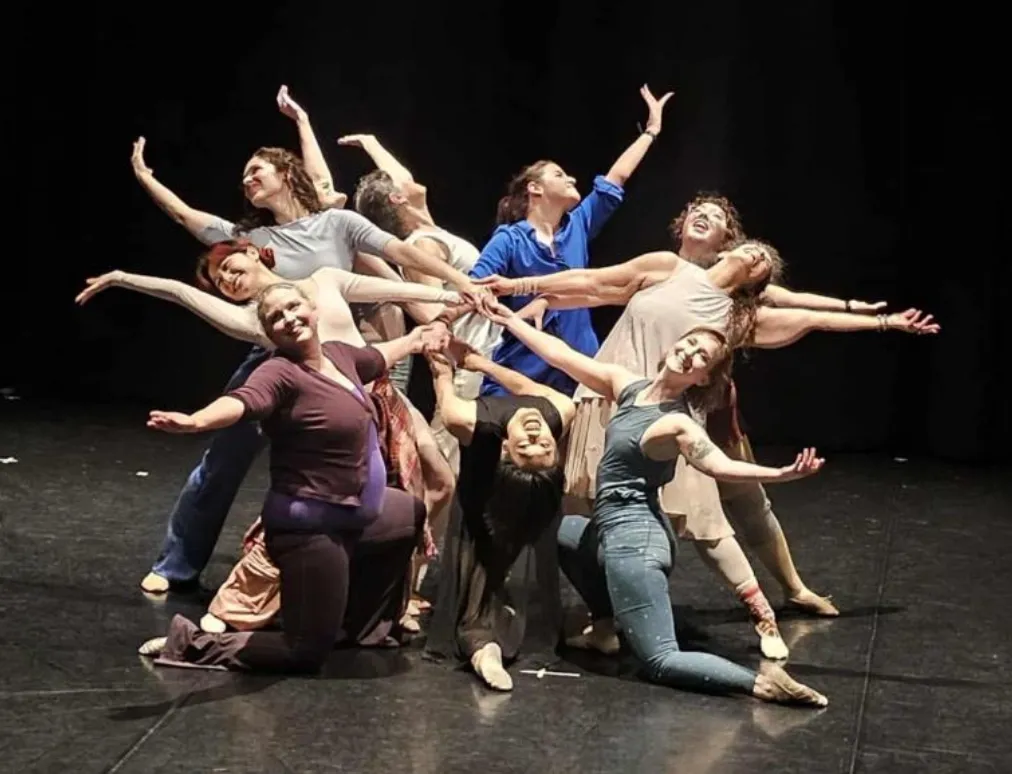 A group of ten dancers holding hands in the middle and extending arms outwards behind them