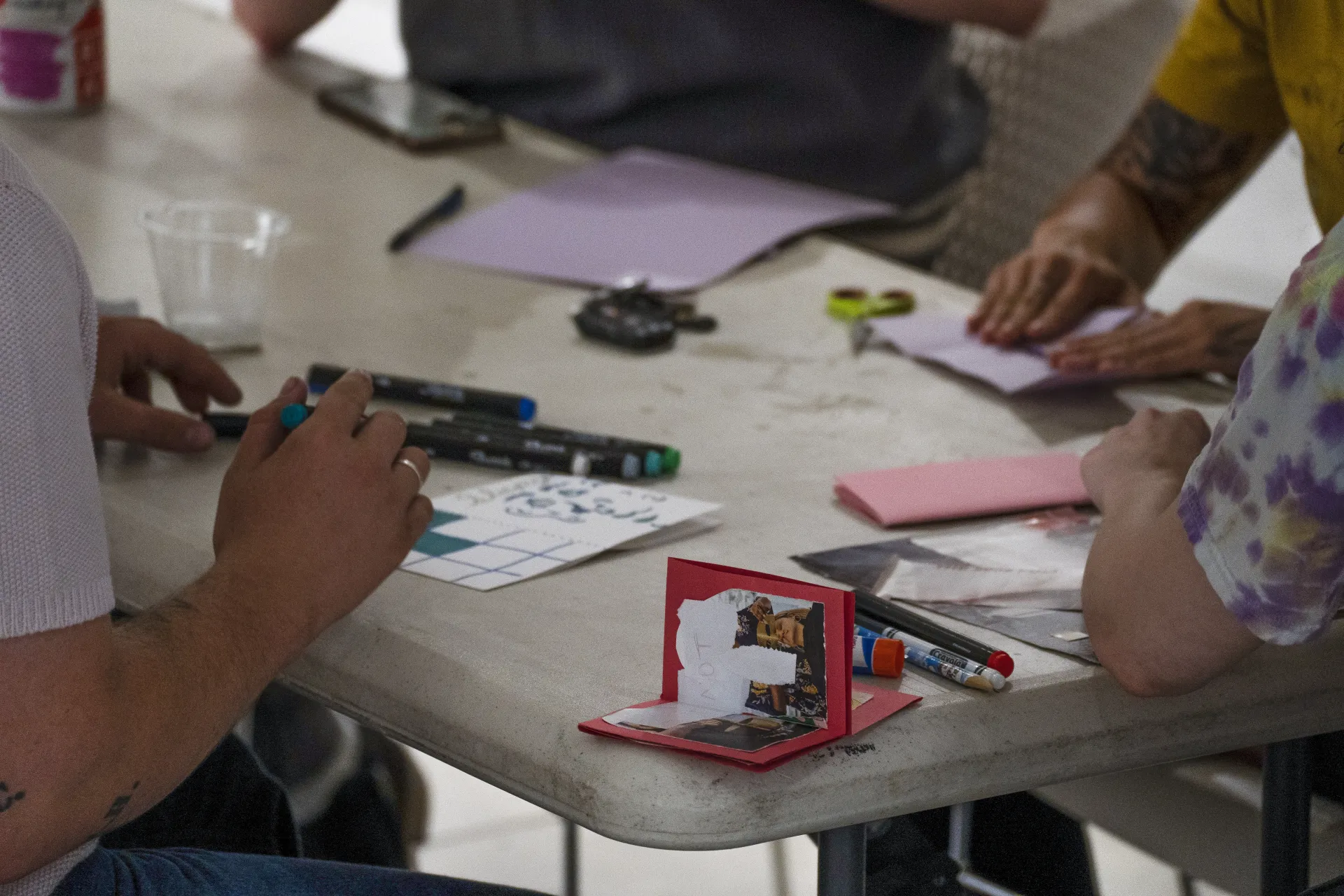 Community members gather around a table with colorful paper, markers, and zines