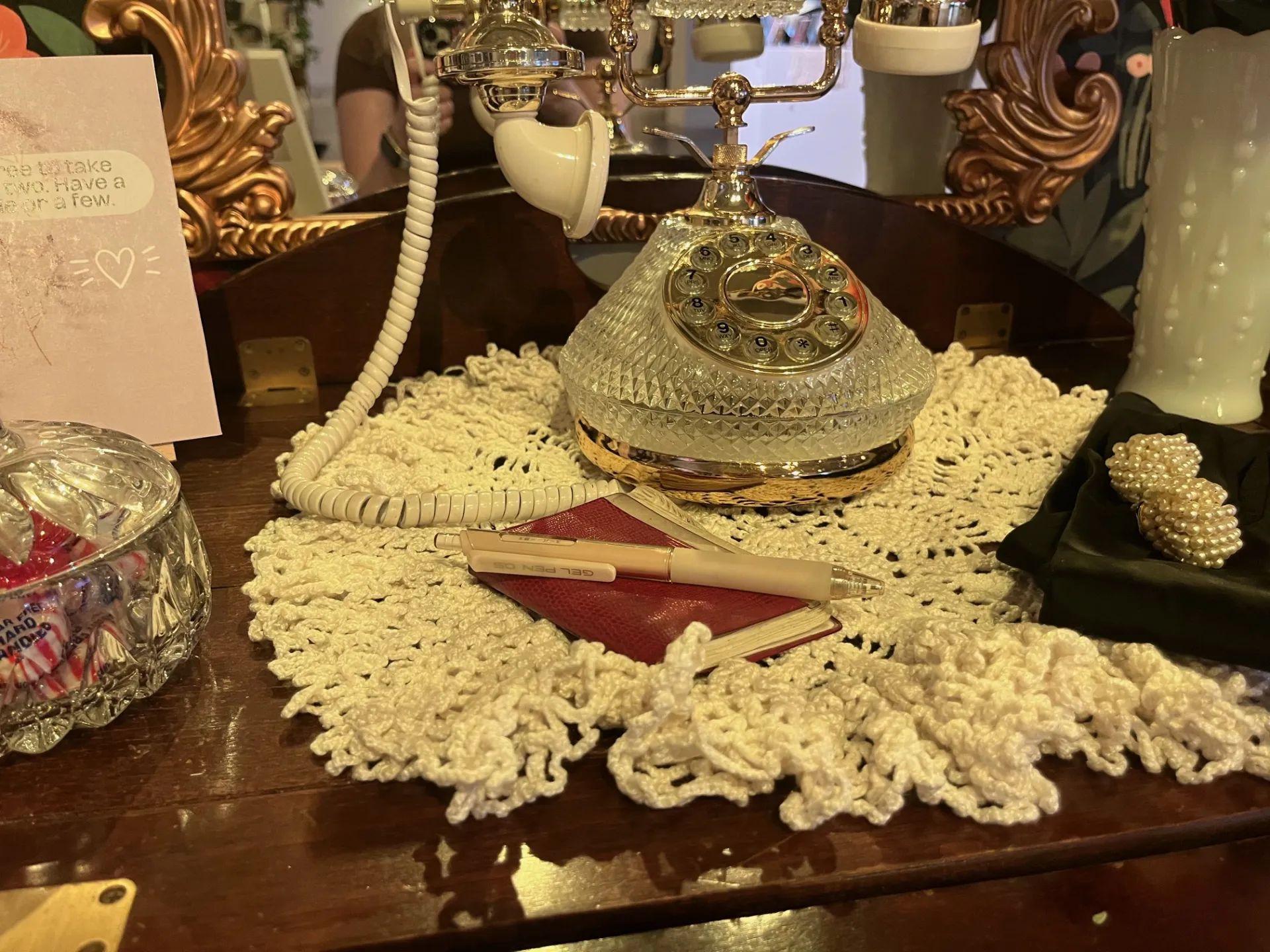 A close-up of a wooden table spread, featuring an antique crystal telephone, a notebook and pen, and a crystal bowl full of peppermints.
