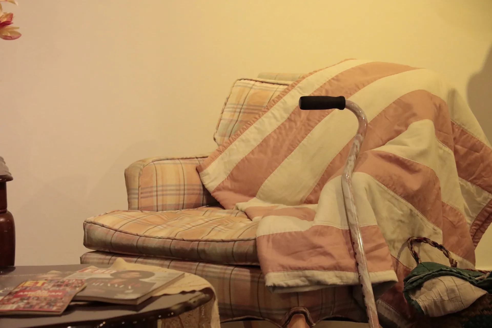 A large armchair covered in a striped blanket with a cane propped up against it. 