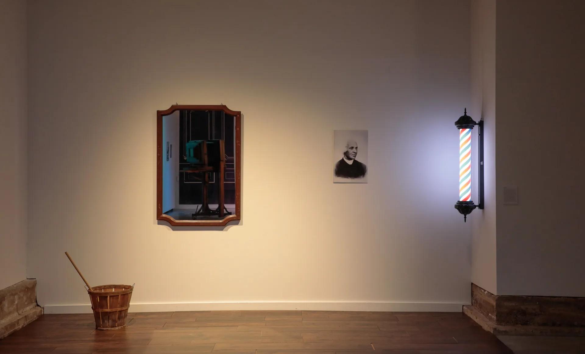 Wooden tiled floor with a basket. On the wall hangs a mirror, a barber pole, and a photo of James Preston Poindexter