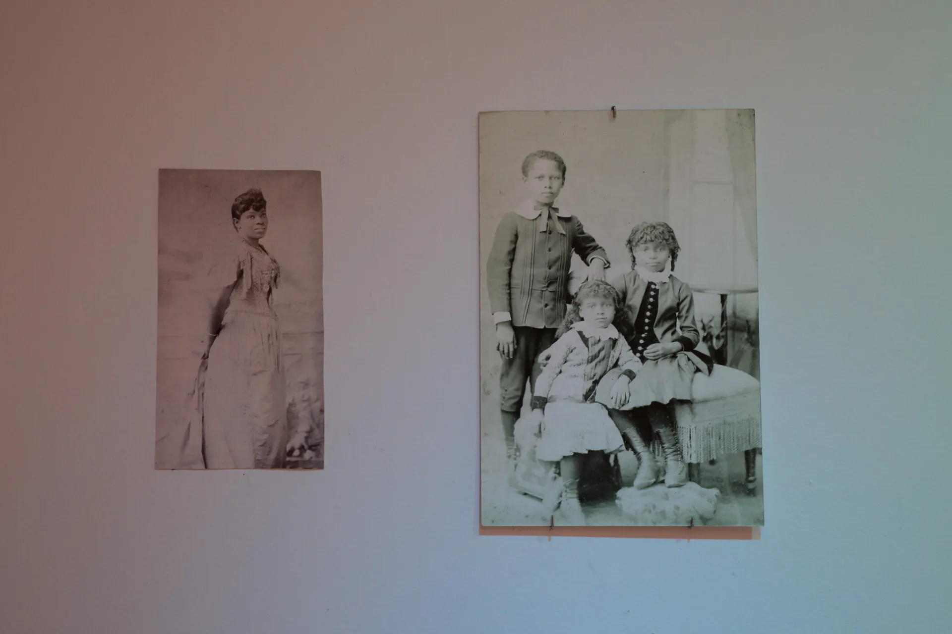 Two vintage photos on the wall, the lefthand photo showing a woman and the righthand showing three children 