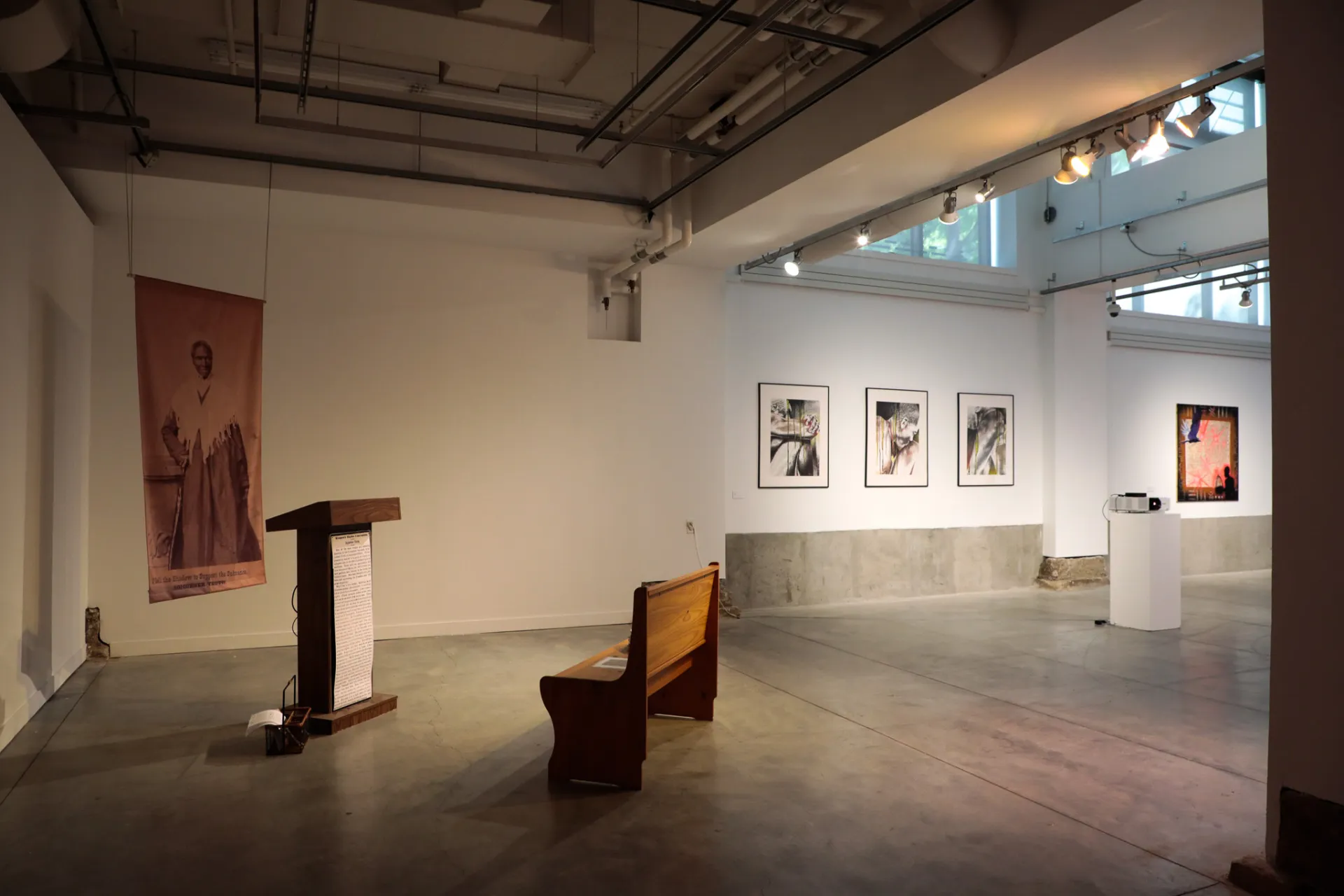The lower gallery with a pew and banner of Sojourner Truth and three paintings 