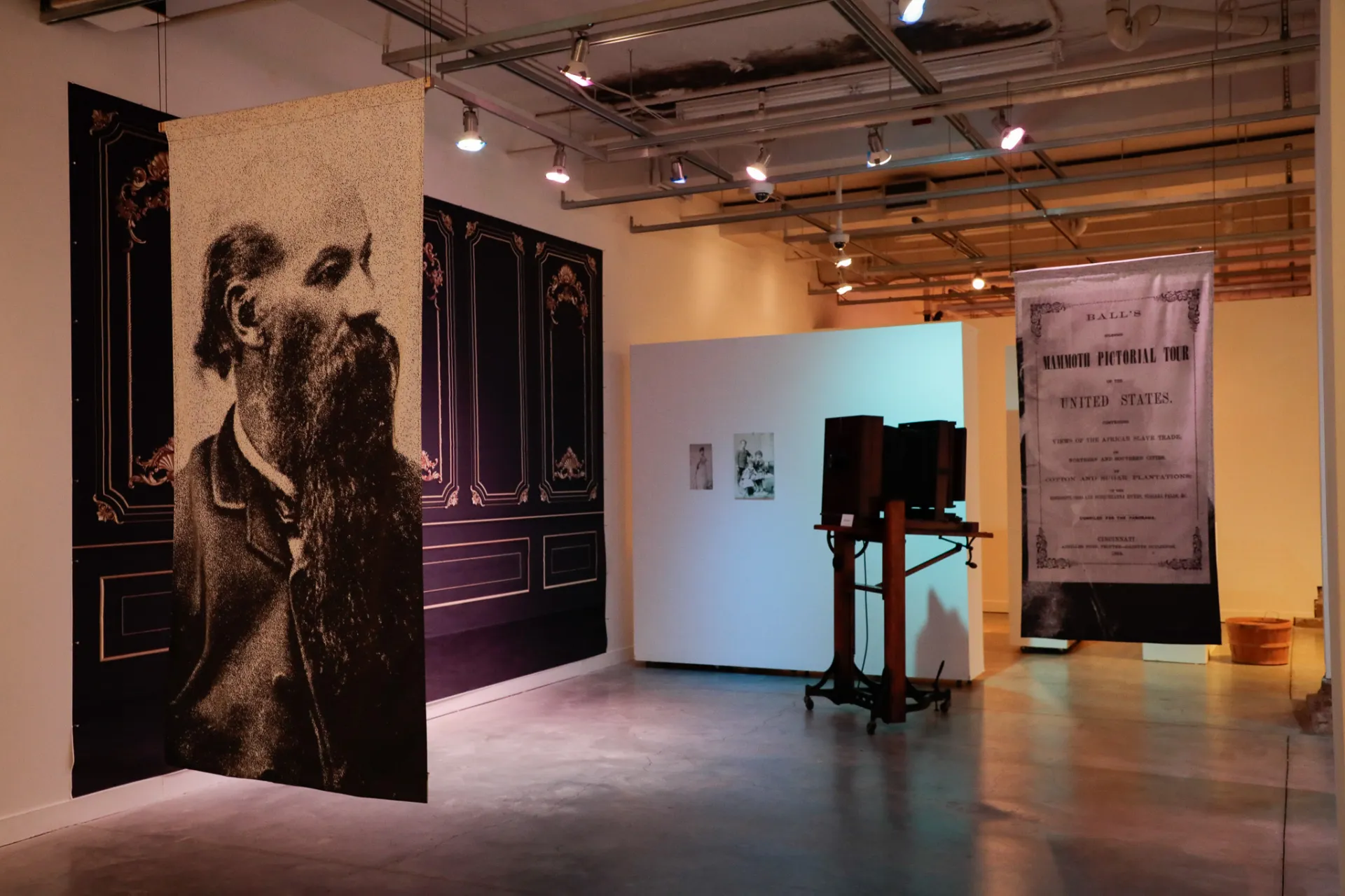 Two hanging banners with pictures of James Presley Ball and a pamphlet from his tour. A camera is in the background.  