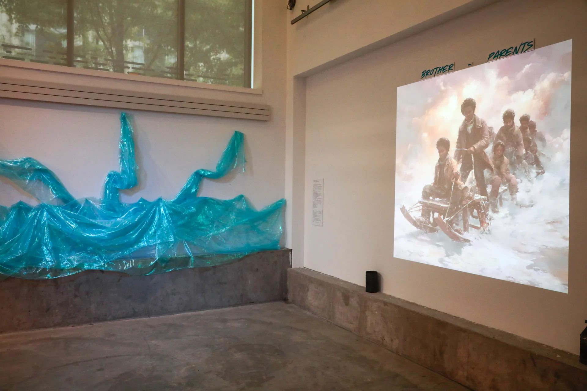 Blue fabric is attached to the lefthand wall to form a wave. An image of boys on sleds is projected on the righthand wall. 