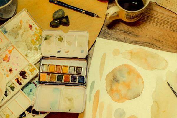 A watercolor palette and painting sit on a desk