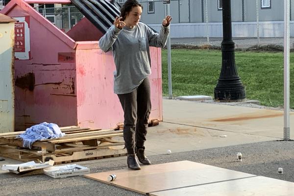 A woman performs a tap dance in front of a dumpster.