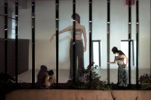 figures mid-dance, a pre-recorded video of them dancing is also being projected on the wall behind them